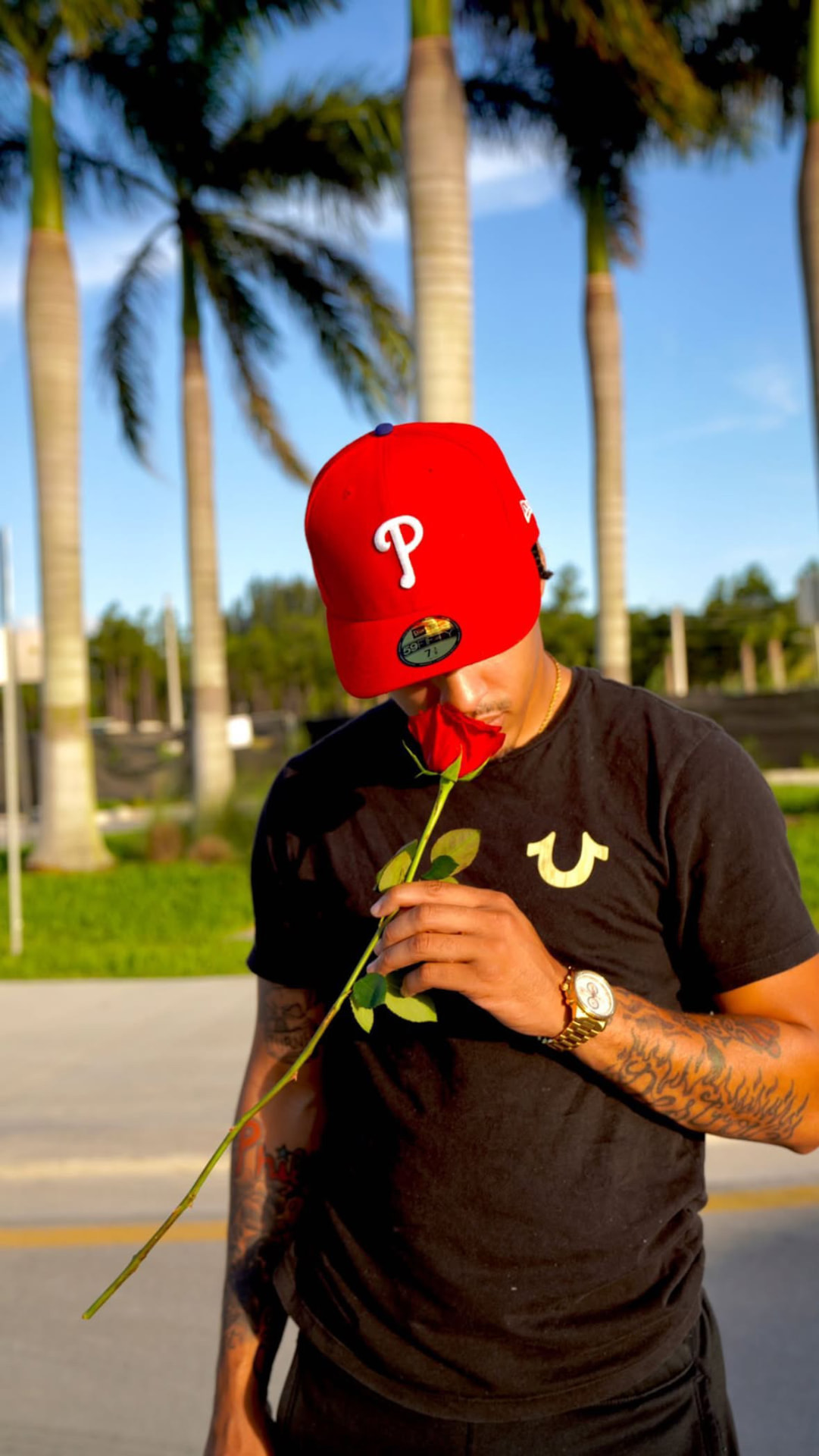 Worth Too Much in a red fitted cap holding a single red rose